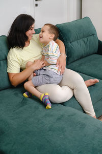 Mother holding child living with disability on sofa woman hugging boy with cerebral palsy at home