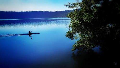 Silhouette man on boat in lake against sky