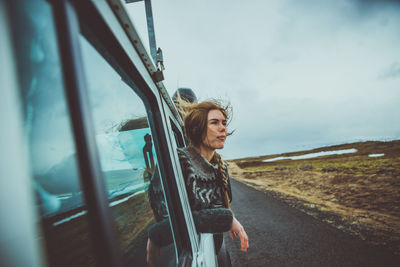 Man looking at camera while standing by road against sky