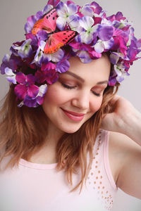 Beautiful young woman wearing flower with butterfly on head against wall