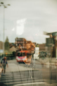 Thoughtful creative professional wearing headphones seen through glass window at office