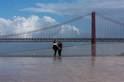 People on suspension bridge against cloudy sky