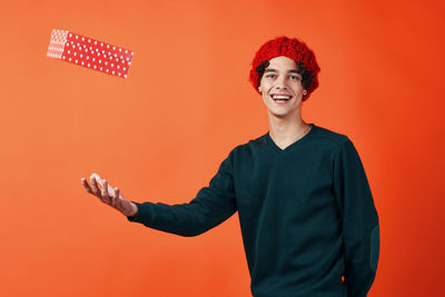 Portrait of young man tossing gift box against colored background