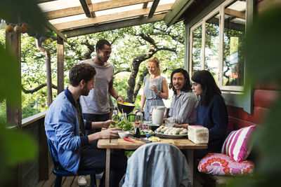 Multi-ethnic friends having food on porch at log cabin during summer party