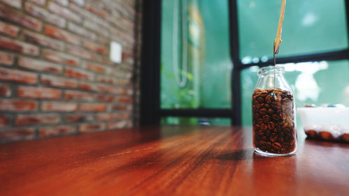 Close-up of glass jar with coffee beans on table against wall