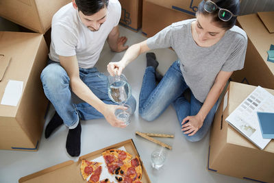 Woman serving water to man while having pizza during relocation of new house