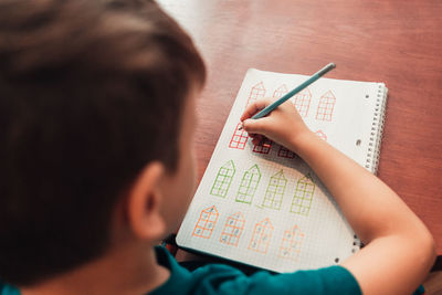 Close up view from above to schoolboy doing math developing creative exercises