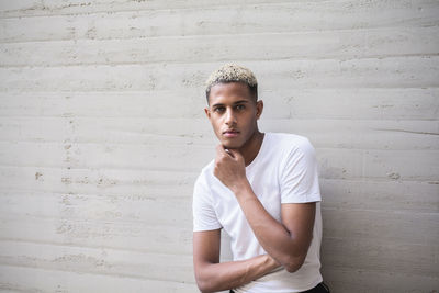 Young man looking away while standing against wall