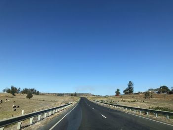 Empty road along landscape against clear blue sky