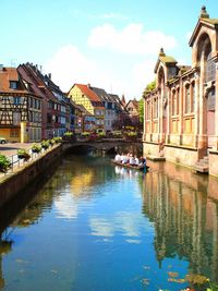 People in boat on canal amidst buildings against sky