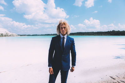 Portrait of man wearing suit standing at beach against sky