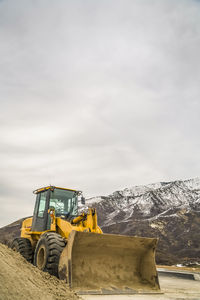 Construction site by snowcapped mountain against sky