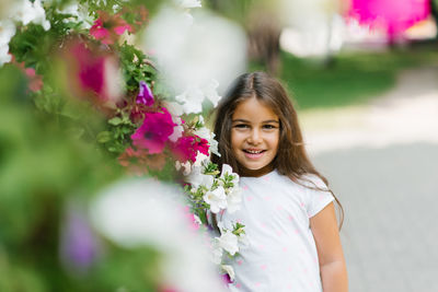 Cheerful little girl smiles among the flowers in summer