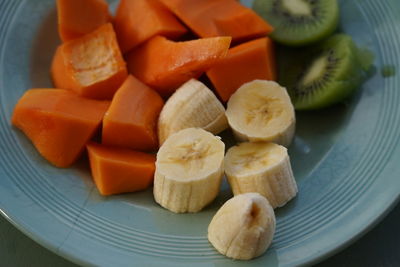 High angle view of chopped fruits in plate on table, mix of banana, papaya and kiwi