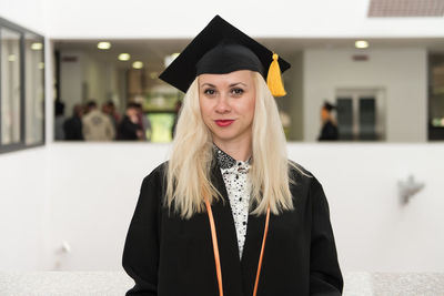 Young woman wearing graduation gown standing against wall