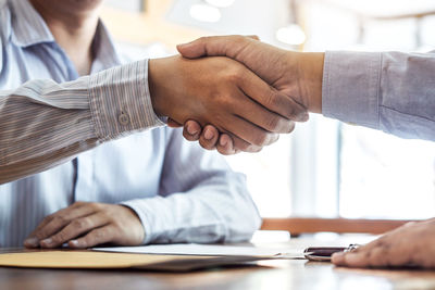 Cropped hand of businessman shaking hand with coworker in office