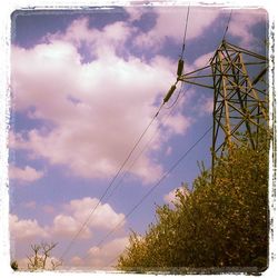 Low angle view of electricity pylon against cloudy sky