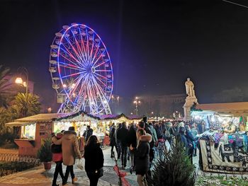 Rear view of people at amusement park against sky at night