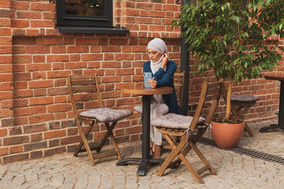 Full length of woman sitting against brick wall