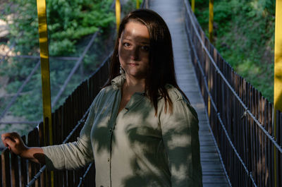 Portrait of young woman standing by railing