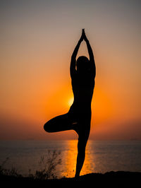 Silhouette woman doing yoga at beach against sky during sunset