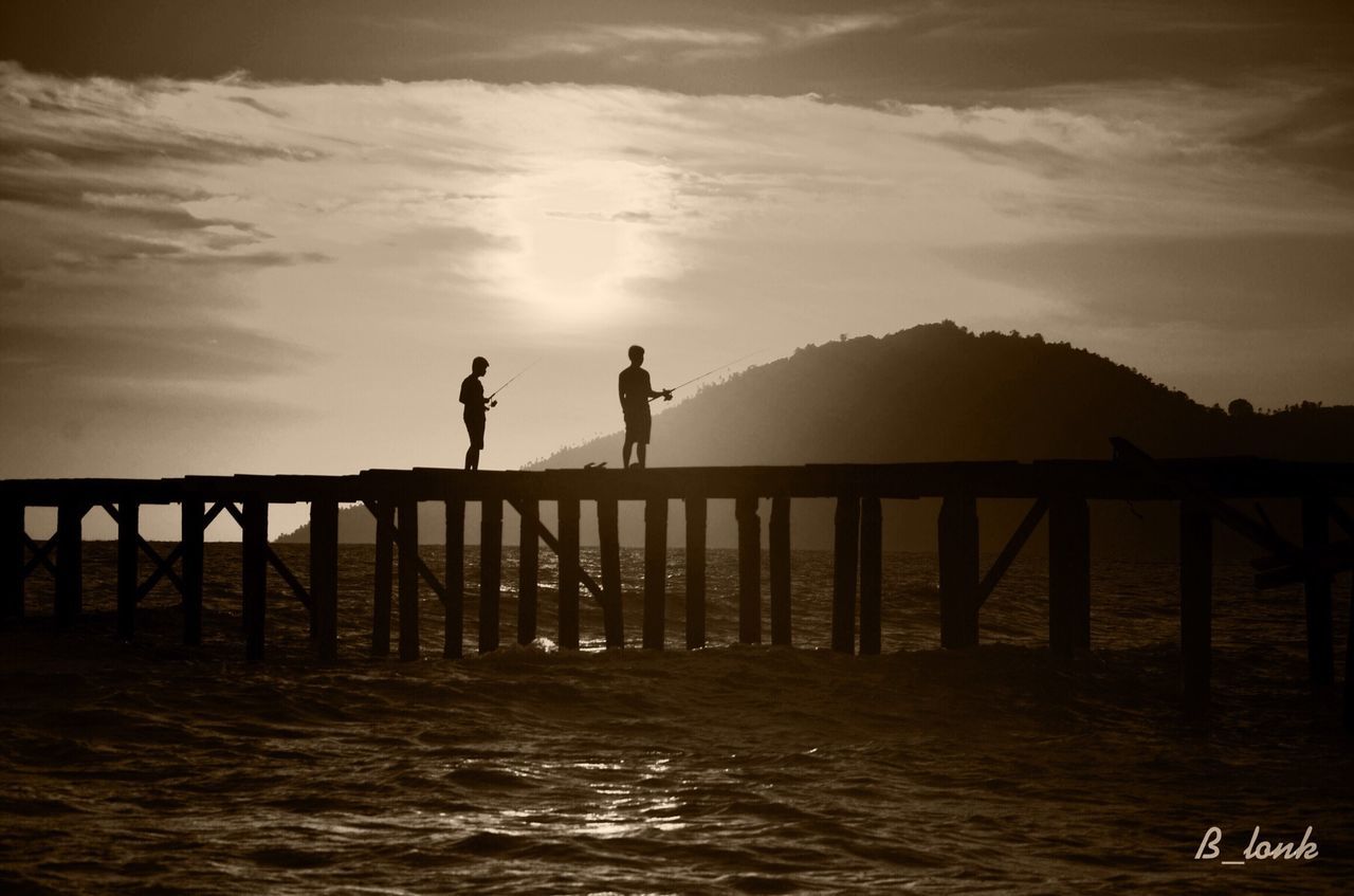 water, lifestyles, men, leisure activity, sky, railing, pier, sea, full length, silhouette, sunset, togetherness, standing, walking, person, bridge - man made structure, rear view