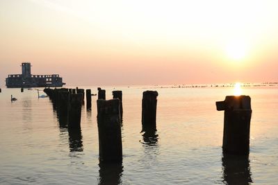 Wooden posts in sea against sky during sunset