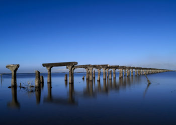 Broken pier on sea against clear blue sky