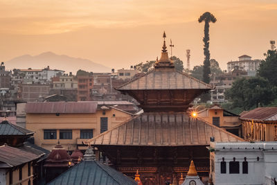 Temple and buildings in city against sky during sunset