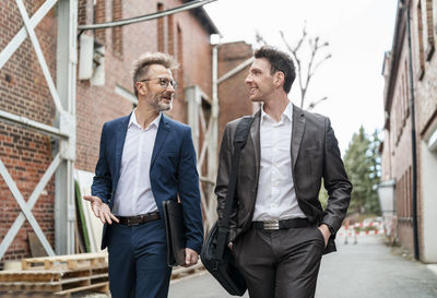Two smiling businessmen walking and talking at an old brick building