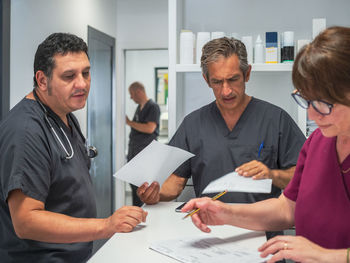 Group of medical practitioners filling and reading documents near counter in modern hospital