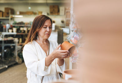 Brunette middle aged woman in white dress buys clay flower pots at hardware store