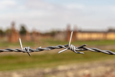 Close-up of barbed wire fence on field against sky