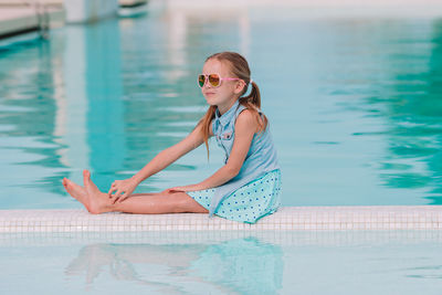 Full length of girl sitting by swimming pool