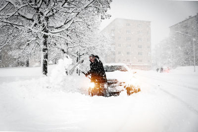 Man shoveling snow while standing by car in city