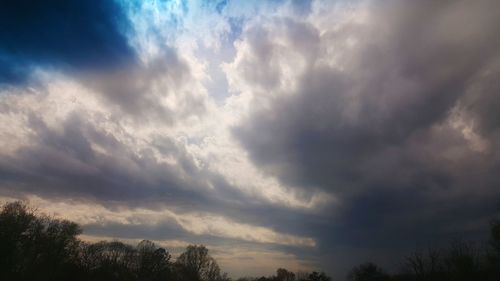 Low angle view of trees against dramatic sky