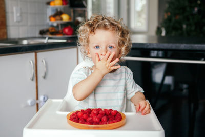 Baby boy eating ripe red fruits at home. supplementary healthy finger food for toddler kids.