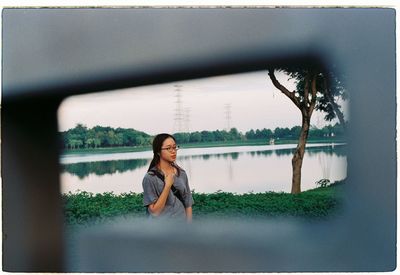 Portrait of woman sitting by lake against sky