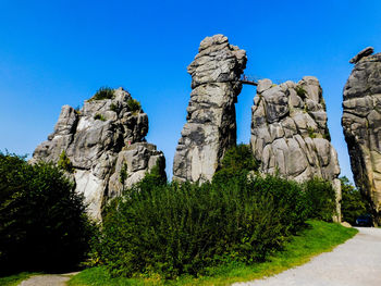 Plants growing by rock formations against clear blue sky