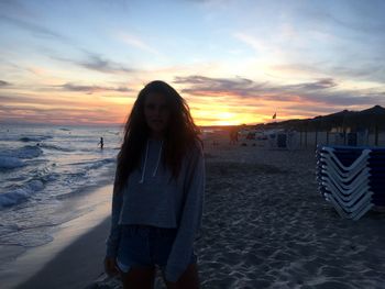 Portrait of woman standing at beach against sky during sunset