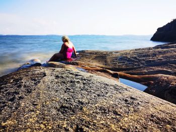 Woman sitting on rock at beach against sky