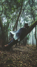 Side view of man lying on tree in forest