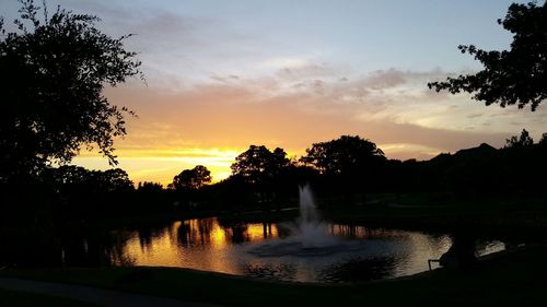 Silhouette trees by lake against sky during sunset