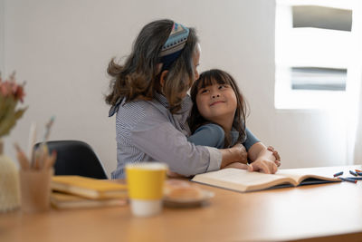 Mother embracing daughter while studying at home