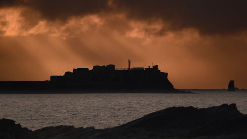 Silhouette buildings by sea against sky during sunset