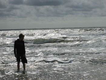 Rear view of boy on beach against sky