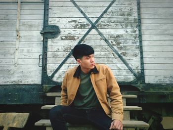 Young man sitting on steps against freight train