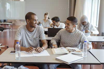 Smiling male friends talking while learning in classroom at high school