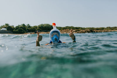 Portrait of woman wearing snorkel showing thumbs up swimming in sea