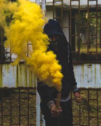 Close-up of man holding yellow distress flare against fence